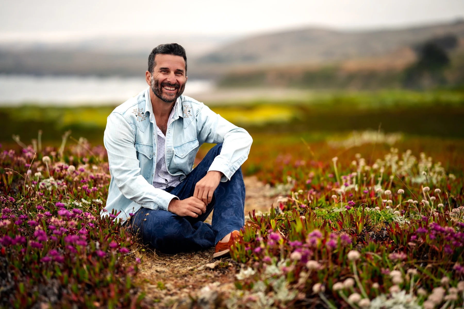 Zev Schiller sitting among coastal wildflowers
